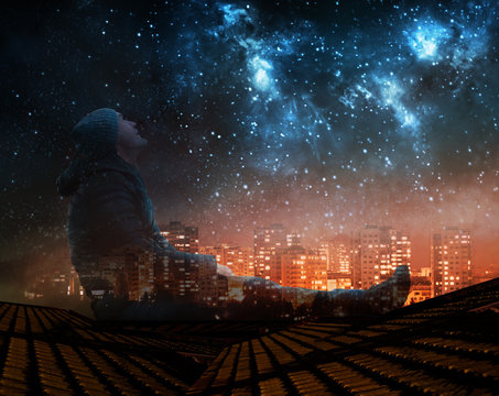 a man watching the stars in night sky on roof in city