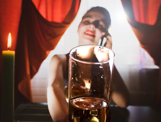 Beautiful girl holding a glass of champagne, drinking champagne in a restaurant, in an evening shiny dress, on a date or a meeting, looking into the camera and tries to touch it. Selective focus