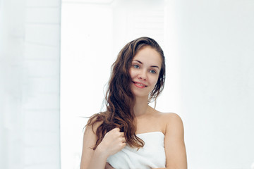 Obraz na płótnie Canvas Hair and body care. Woman touching hair and smiling while looking in the mirror.Portrait of happy girl with wet hair in bathroom applying conditioner and oil. Girl uses protection moisturizing cream