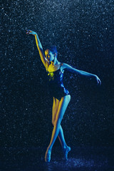 Young female ballet dancer performing under water drops and spray. Caucasian model dancing in neon...