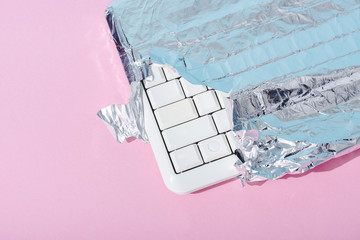 top view of computer keyboard wrapped in silver foil on pink, Chocolate Bar concept