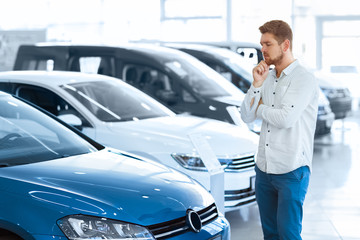 Final decision. Shot of a handsome young man standing in front of a new car at the dealership...