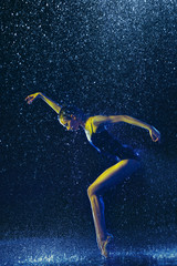 Young female ballet dancer performing under water drops and spray. Caucasian model dancing in neon...