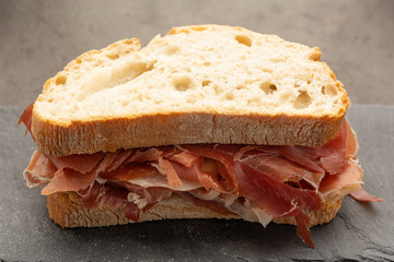 tasty Spanish ham on bread over dark background