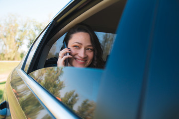 Positive businesswoman using phone and looking through car window