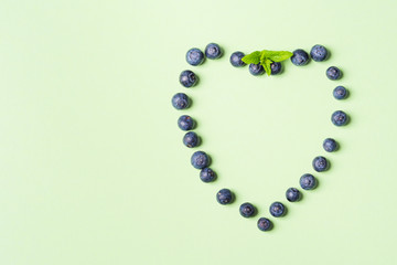 Fresh blueberries in shape of heart frame on pastel green background. Healthy breakfast concept