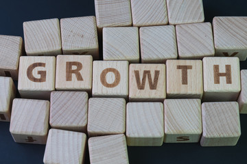 Business growth, company expand to get more revenue concept, cube wooden block with alphabet building the word Growth at the center on dark blackboard background, new opportunity in career path