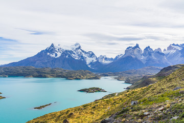 Naklejka na ściany i meble Beautiful panoramic view of golden grass and aqua blue Pehoe lake with small island with nature cuernos mountains peak with cloud in autumn, Torres del Paine national park, south Patagonia, Chile