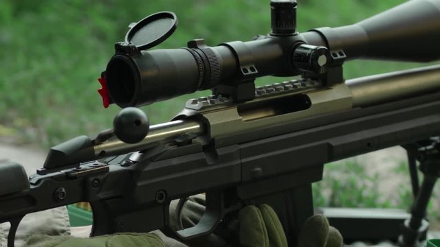 Sniper charges the rifle. A man charges a sniper rifle. Close-up hands. Slow Motion. 4K. UHD