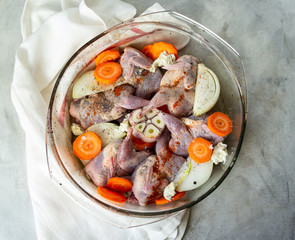Raw meat of quails with vegetables - garlic, carrots, onions in a glass form with a light background. Dietary, gourmet lunch. Close up, selective focus, top view.