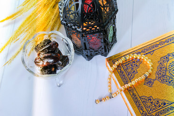 Ramadan lantern, rosary beads, holy quran and dry dates against white background. 