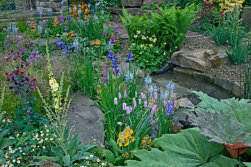 A country cottage and garden situated in a wooded rockery with a colourful display of flowers