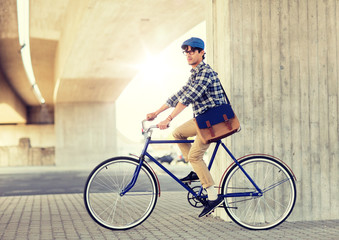 Obraz premium people, style, leisure and lifestyle - young hipster man with shoulder bag riding fixed gear bike on city street