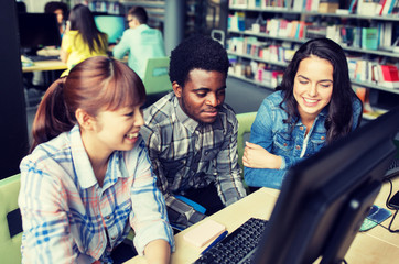 people, education, technology and school concept - group of happy smiling international students with computers at library in university