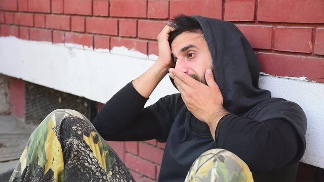 Homeless man, Homeless man drug and alcohol addict sitting alone and depressed on the street leaning against a red brick building wall feeling anxious and lonely, social documentary concept 