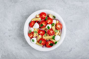 Italian pasta salad with tomatoes, mozzarella cheese, red onion and basil. Top view.