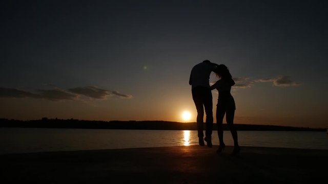 Young boy and girl dance salsa at sunset near the lake. Silhouette shooting.