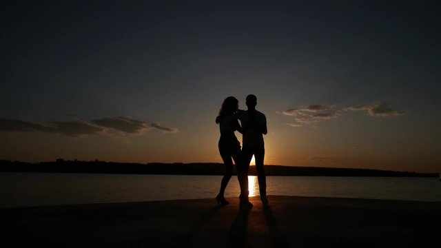 Young boy and girl dance salsa at sunset near the lake. Silhouette shooting. Slow motion