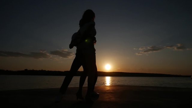 Young boy and girl dance salsa at sunset near the lake. Silhouette shooting.