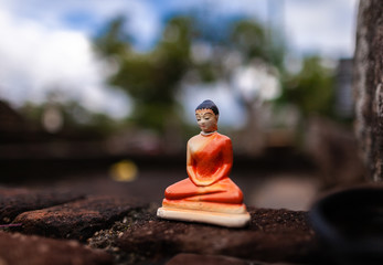 Cheap clay figurine of Buddha left on an old brick wall