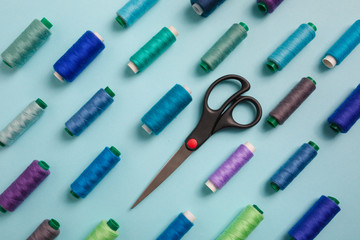 Flat lay composition with sewing threads and scissors on blue background