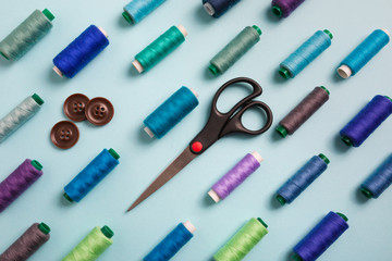 Flat lay composition with sewing threads, scissors and buttons on blue background