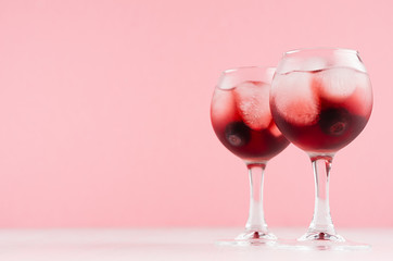 Exquisite red alcoholic shots of sweet berry liquor with ice cubes, blueberry on pastel soft light pink background, copy space.