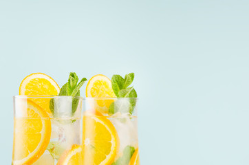 Homemade oranges lemonades with slices, ice cubes, mint in wet wineglasses on blue background,  closeup, top section, edge.