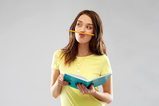 education, school, inspiration and people concept - young woman or teenage student girl in yellow t-shirt with diary or notebook and pencil-mustache over grey background