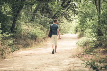 teenager with a bag on his shoulder goes to the forest.