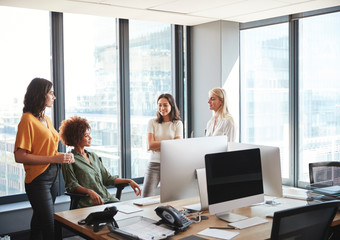 Four female colleagues in discussion at a desk in a creative office, looking at each other