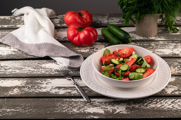 tomatoes and cucumbers salad in a white bowl on a grey rustic backdrop, copy space