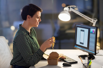 business, deadline and people concept - female graphic designer eating takeaway wok food by chopsticks and working on computer at night office - Powered by Adobe