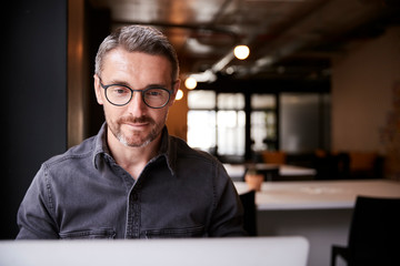 Middle aged white male creative sitting in an office looking at laptop computer screen, close up