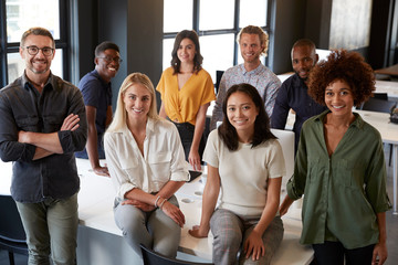 Portrait of a creative business team leaning on a desk, smiling to camera in office, elevated view