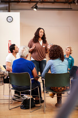 Woman Standing To Address Self Help Therapy Group Meeting In Community Center