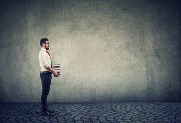 Smart man holding pile of books isolated on gray wall background.