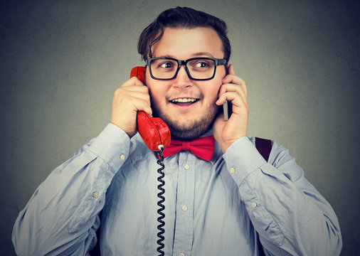 Happy businessman using cellphone and retro style telephone at once