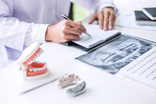 Male doctor or dentist writing report working with tooth x-ray film, model and equipment used in the treatment of dental and dentistry at workplace