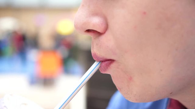 A guy in a fast food restaurant drinks a carbonated sweet drink through a tube. Mouth close up