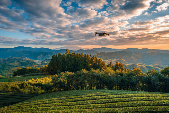 Modern Drone with camera flying over Mt. Fuji with green tea field at sunrise in Shizuoka, Japan.