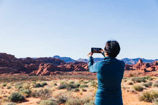 Senior Asian woman taking a photo of a desert landscape with her camera phone in Valley of FIre, Nevada, North America