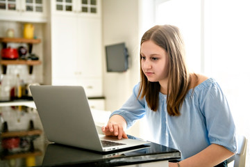 teenager girl using laptop studying in kitchen