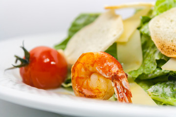 Caesar salad with croutons, cheese, lettuce and grilled shrimps on a white background close-up