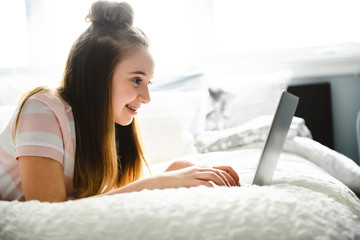 A Young smiling teen girl on bed with laptop