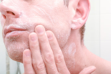 Naklejka premium Man looking in mirror and applying product to skin on face in the bathroom