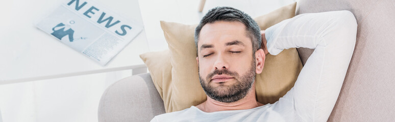 Obraz premium panoramic shot of handsome bearded man with eyes closed resting on couch at home