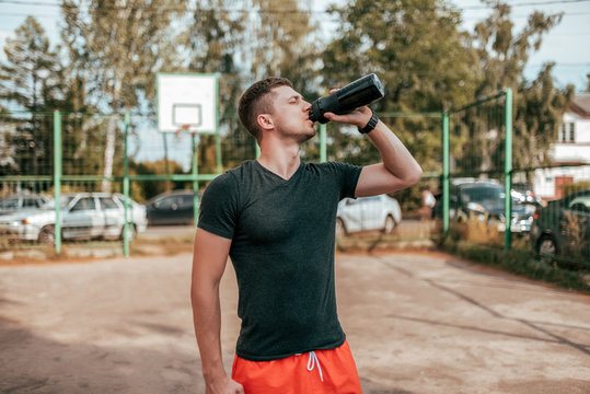 Male athlete, in the summer in the city on the sports ground. In hand a shaker with water and protein. Drinks, resting after a workout fitness in nature. The concept of quenching thirst. Casual wear.