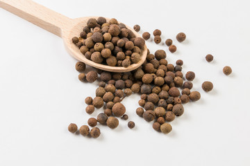 Allspice or Jamaican pepper on wooden spoon on white background