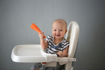 Baby nibbles carrot on baby chair, fresh vegetable